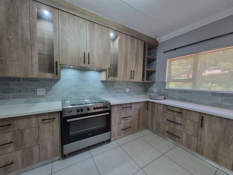 Modern kitchen featuring wood-grain cabinetry, stone-look countertops, subway tile backsplash, and a stainless steel gas stove with an integrated extractor fan.