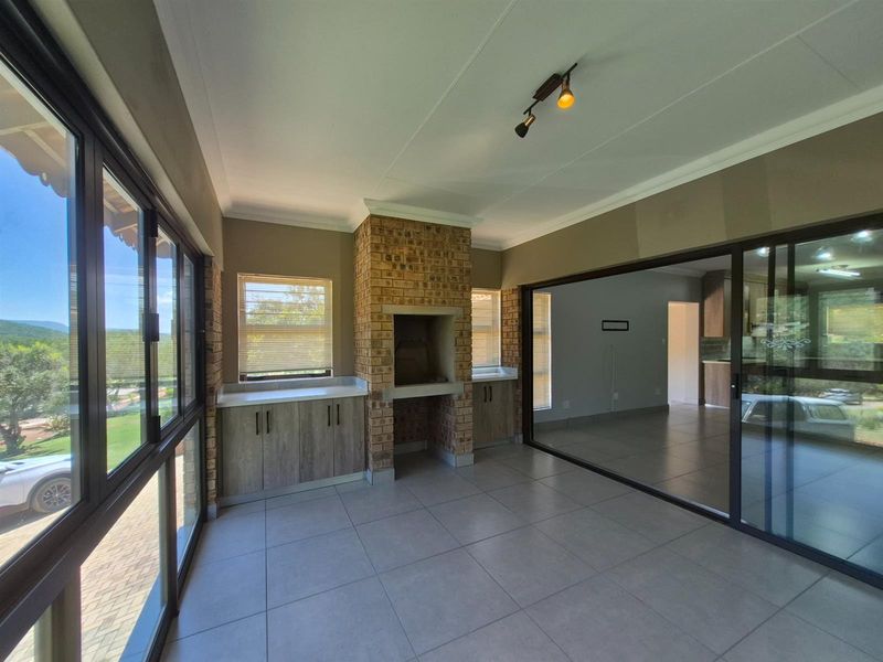 Enclosed patio area featuring a built-in brick braai, tiled flooring, and large sliding glass doors providing ample natural light and garden views.