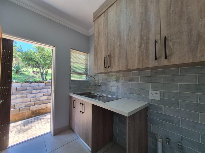 A functional laundry area featuring wood-look cabinetry, a stainless steel sink, subway tile backsplash, and direct access to the rear garden.