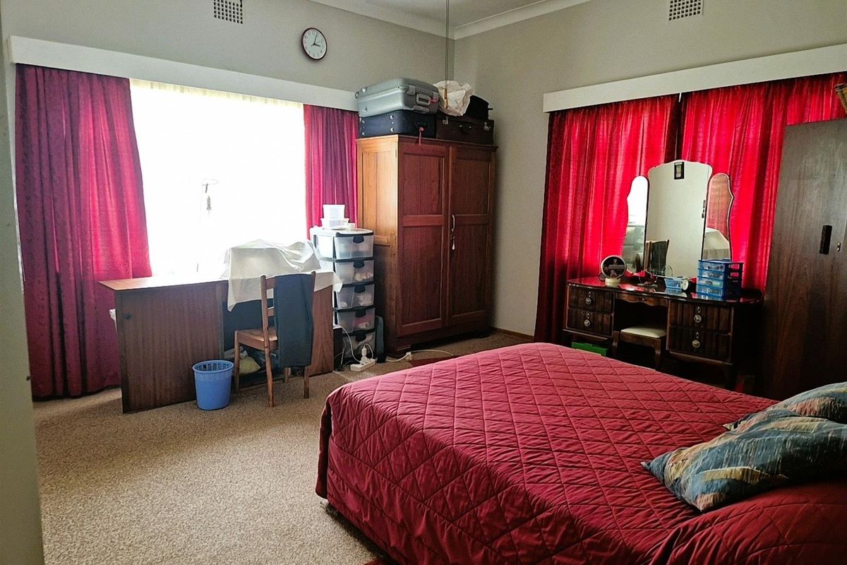 A spacious bedroom featuring neutral wall finishes, carpeted flooring, and large windows with curtain tracks.