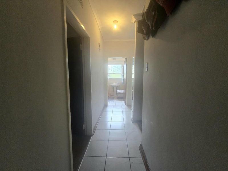 A narrow residential hallway featuring tiled flooring and neutral wall finishes, providing access to adjacent rooms including a bathroom with a pedestal basin.