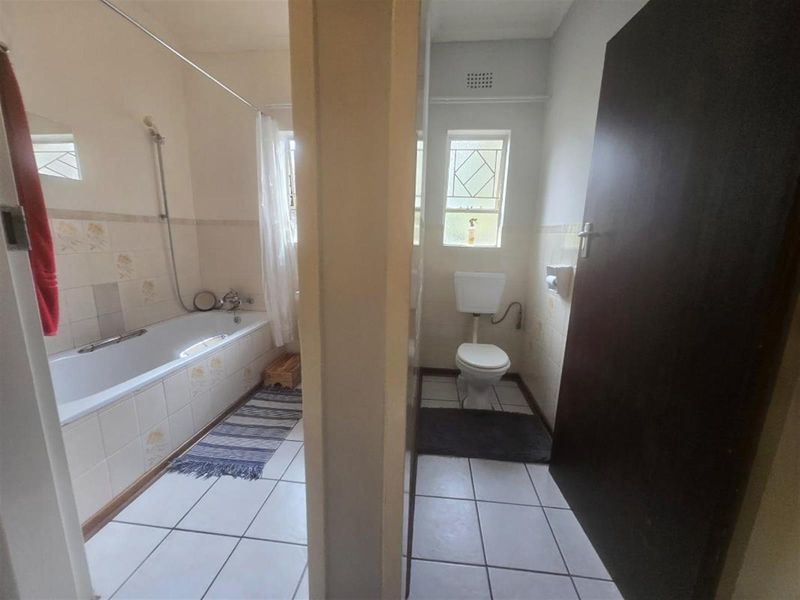 A functional bathroom featuring a separate bathtub area and a private toilet cubicle with tiled finishes and natural light.