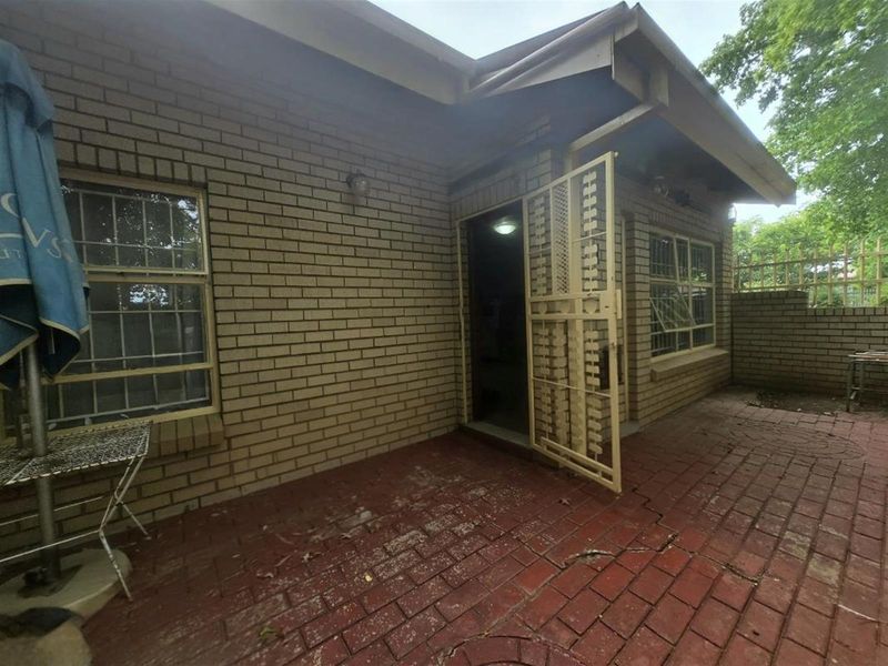 Rear exterior view of the townhouse featuring a paved patio area, brick facade, and security gate access.