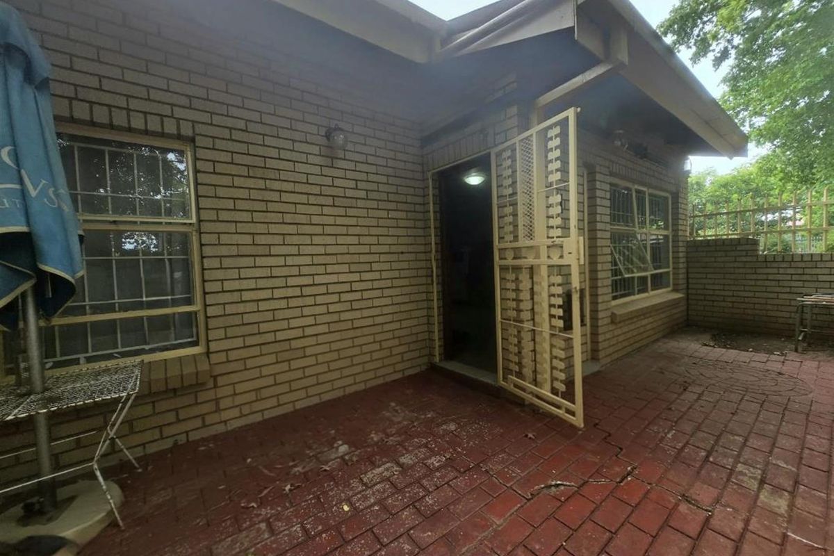 Rear exterior view of the townhouse featuring a paved patio area, brick facade, and security gate access.