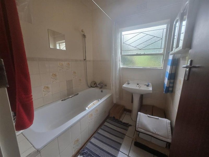 A dated bathroom featuring a standard bathtub with shower mixer, pedestal basin, and tiled finishes, offering potential for a modern renovation.