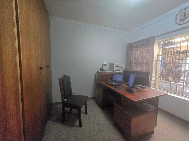 A functional home office featuring carpet flooring, a built-in wardrobe, and a window fitted with security bars.