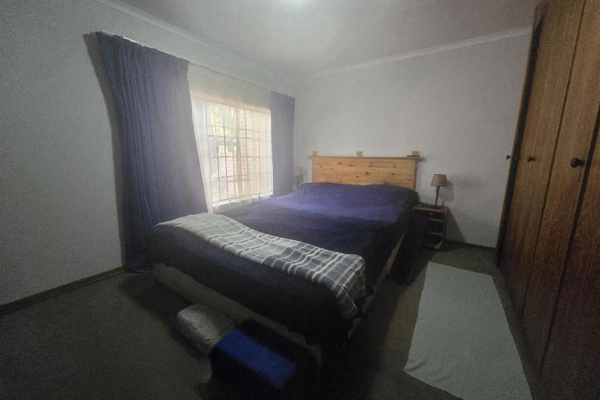 A standard bedroom featuring built-in wooden cupboards and a window fitted with security burglar bars.