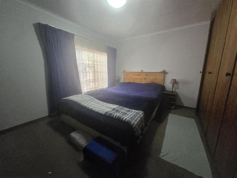 A standard bedroom featuring built-in wooden cupboards and a window fitted with security burglar bars.
