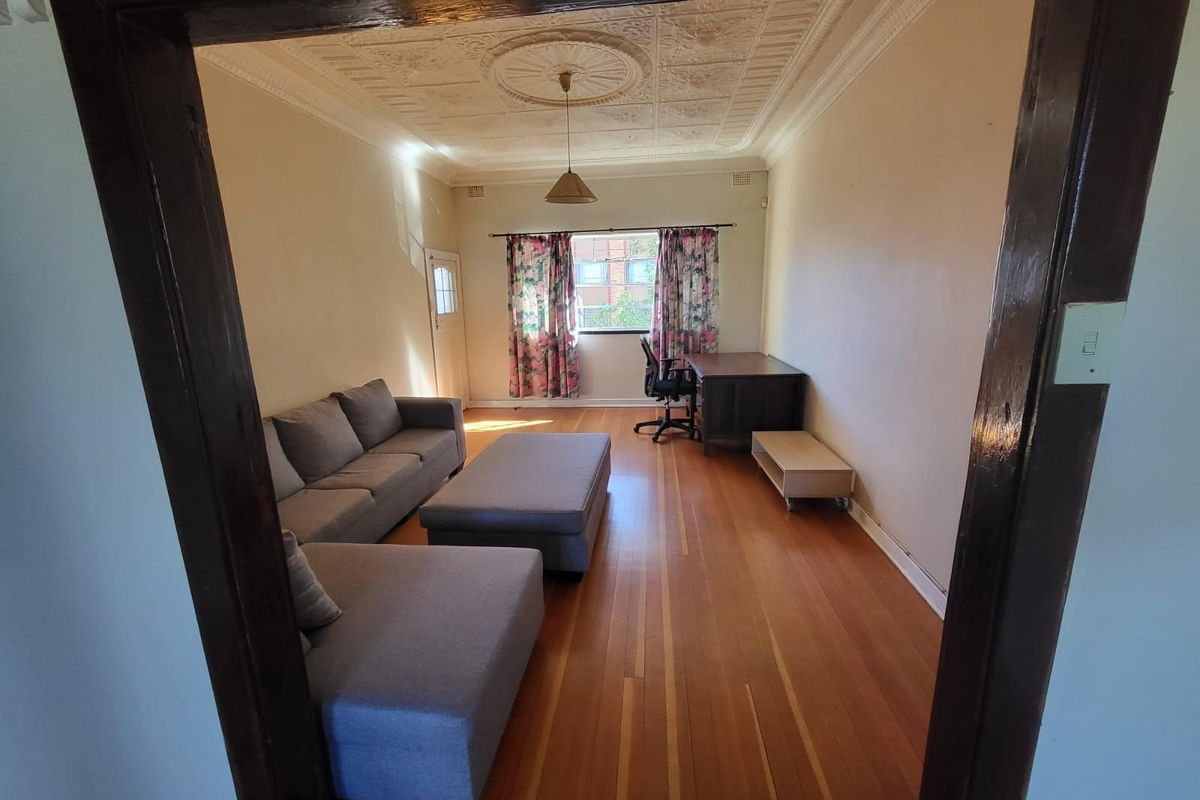 Spacious living room featuring original decorative pressed metal ceiling, polished timber flooring, and natural light through a large window.