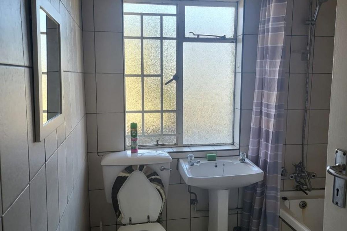 A compact bathroom featuring a pedestal sink, toilet, and a shower-over-bath combination with full-height wall tiling.