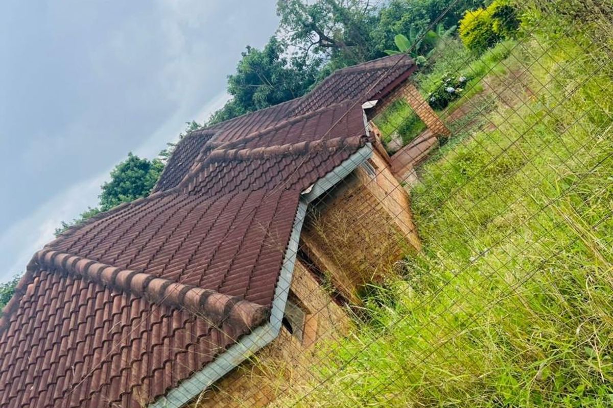 An exterior view of a residential property featuring a tiled roof and brick facade, set within an overgrown garden area.