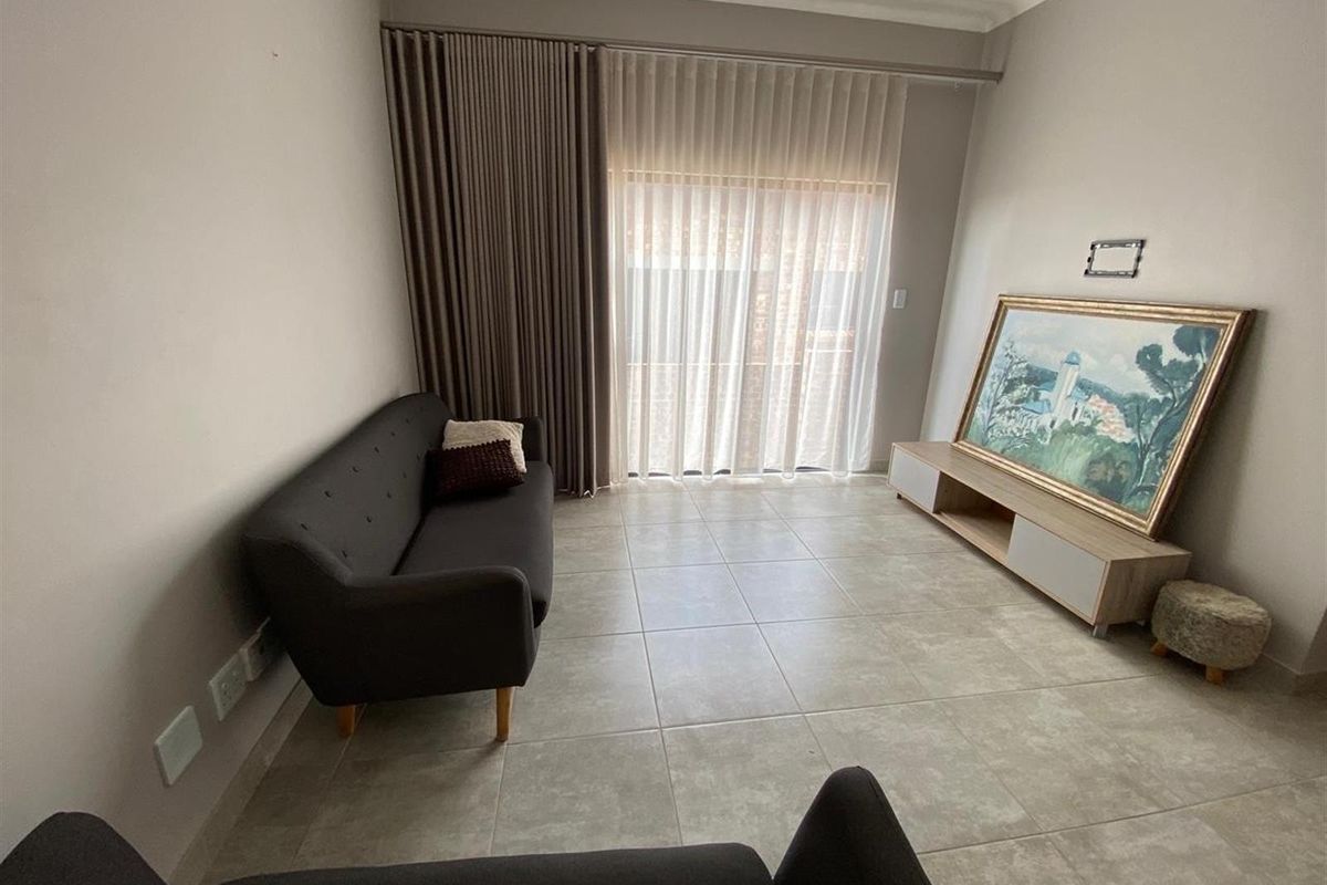 A bright living room featuring neutral floor tiles, large sliding glass doors with floor-to-ceiling curtains, and a clean, minimalist aesthetic.