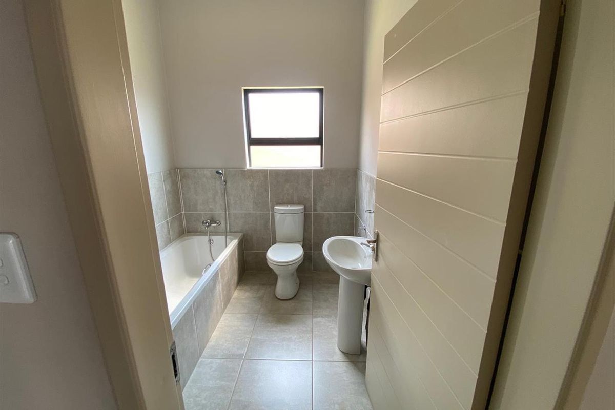 A clean and functional bathroom featuring a bathtub with shower attachment, pedestal basin, and toilet with neutral floor and wall tiling.
