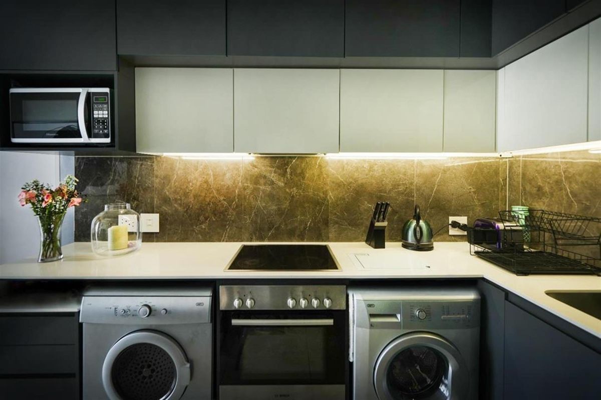 Modern kitchen featuring sleek cabinetry, stone countertops, integrated oven and hob, and under-cabinet lighting, with dedicated space for laundry appliances.