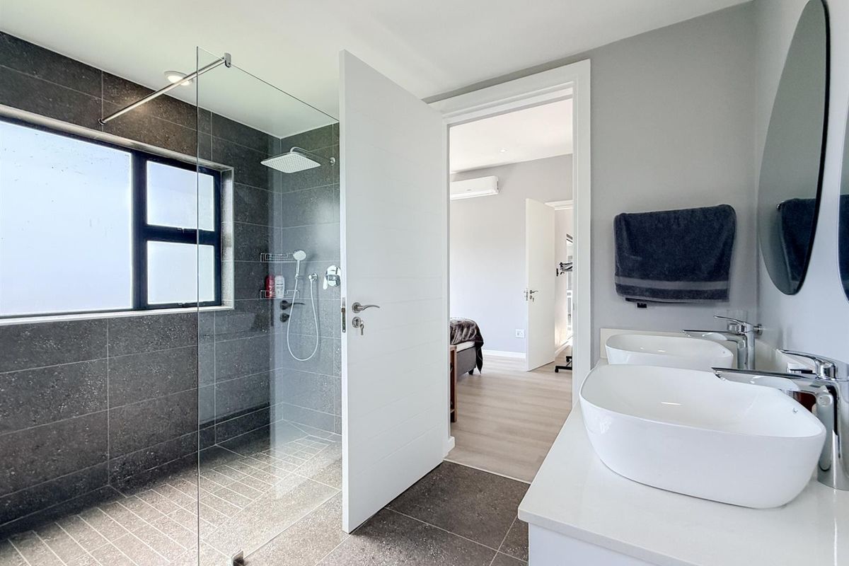Modern bathroom featuring a spacious walk-in shower with dark tiling, a double vanity with vessel sinks, and contemporary fixtures.