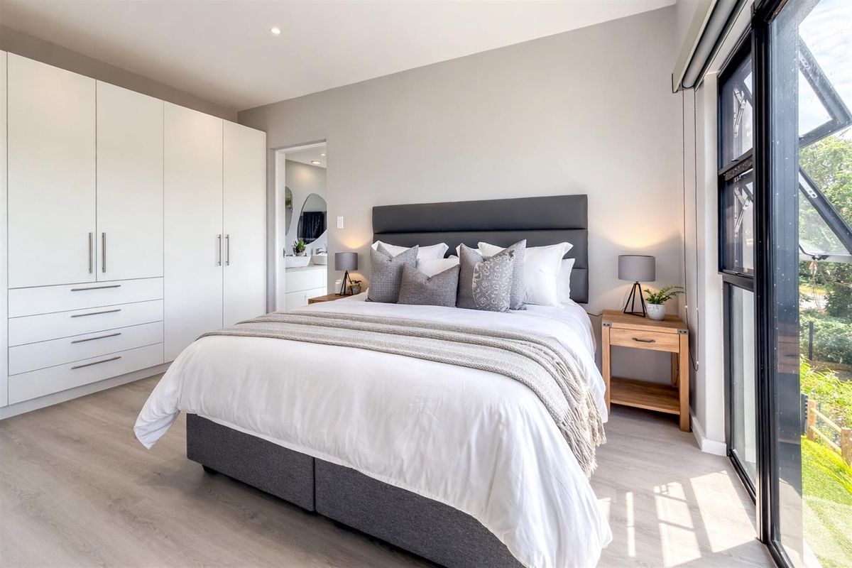 Modern bedroom featuring light laminate flooring, ample built-in cupboard space, and large windows allowing for natural light.