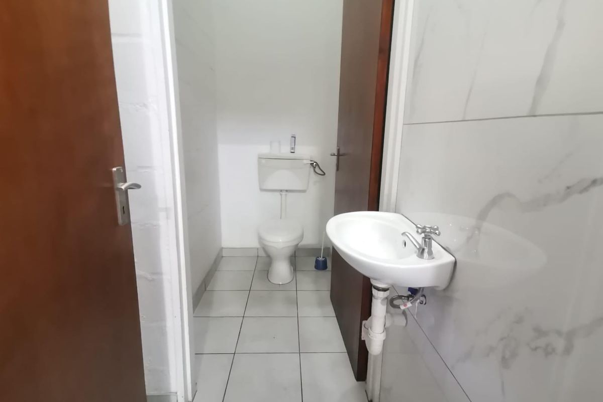 A compact bathroom featuring a wall-mounted basin and a standard toilet, finished with white marble-look wall tiles and neutral floor tiling.
