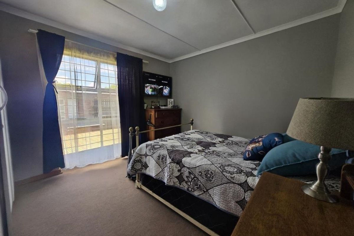 A standard bedroom featuring carpeted flooring, ceiling tiles, and a window fitted with security bars.