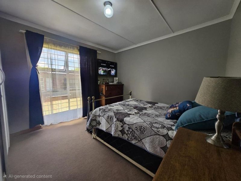 A standard bedroom featuring carpeted flooring, ceiling tiles, and a window fitted with security bars.