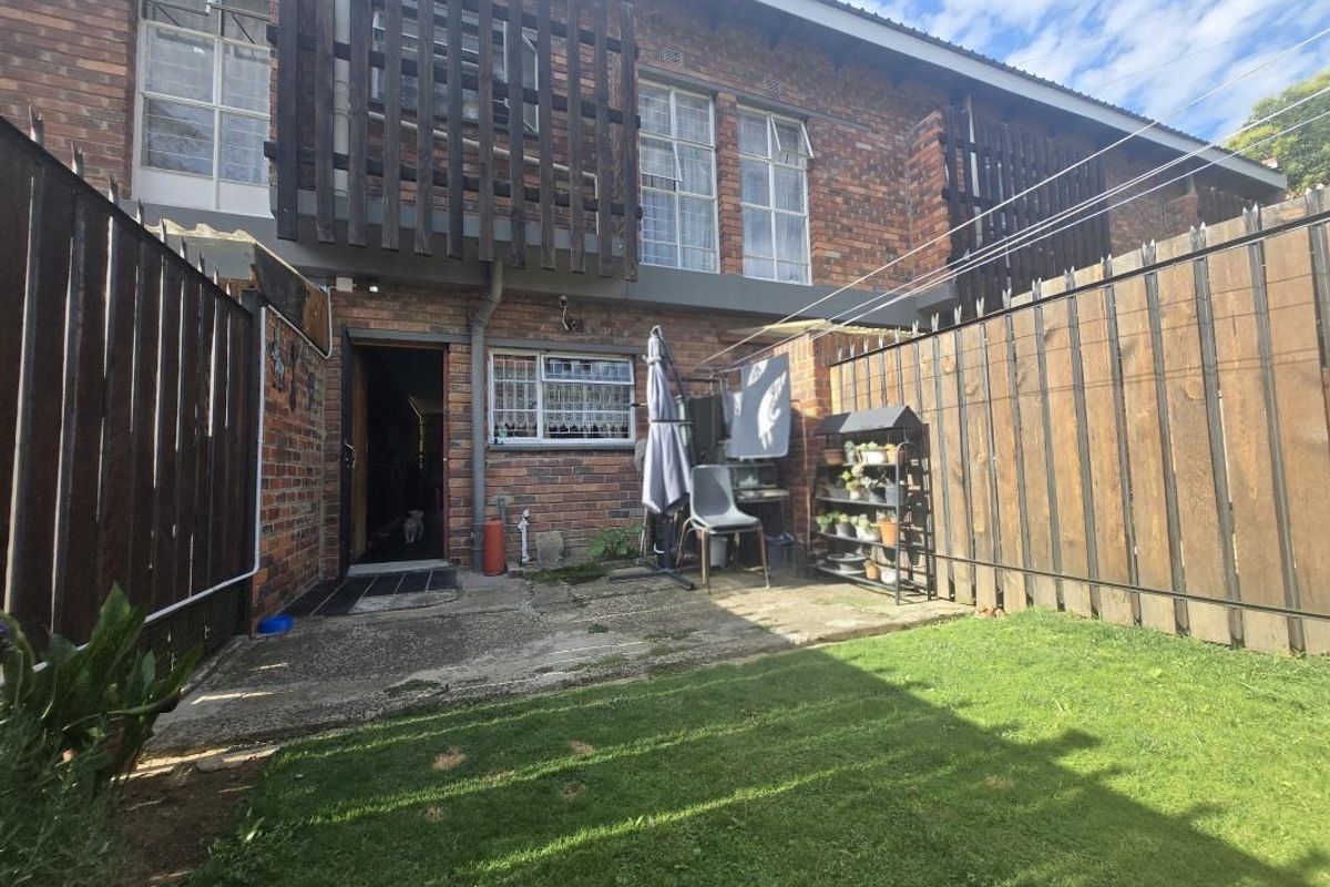 Rear exterior view of a townhouse featuring a brick facade, private garden area with lawn, and a concrete patio space.