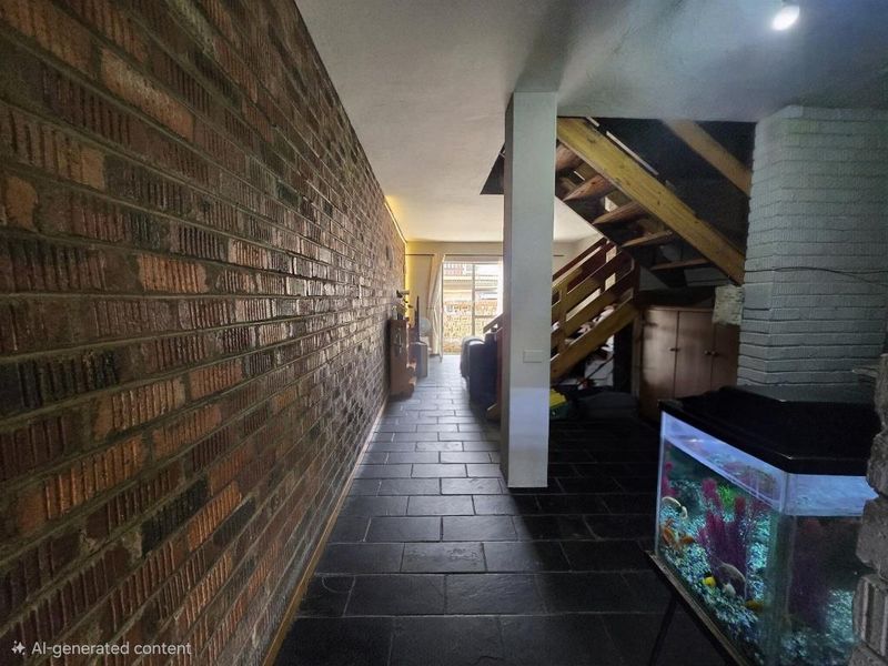 A hallway featuring an exposed brick wall, dark stone tile flooring, and a wooden staircase leading to the upper level.
