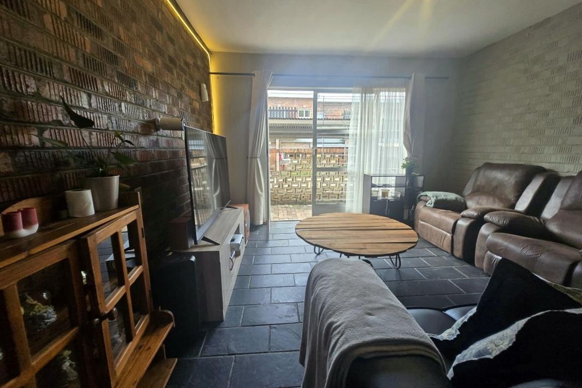 A living room featuring exposed brick walls, slate tile flooring, and a sliding glass door providing access to the outdoor area.