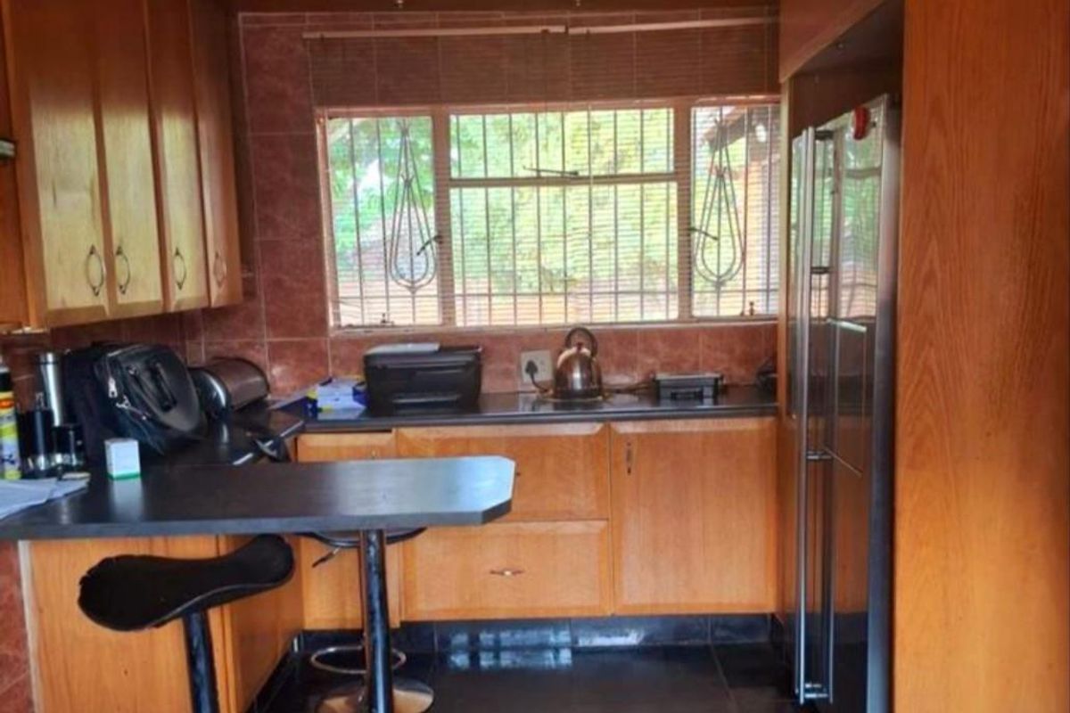 A functional kitchen featuring wood-veneer cabinetry, dark countertops, a breakfast bar, and dark floor tiles with a window overlooking the exterior.