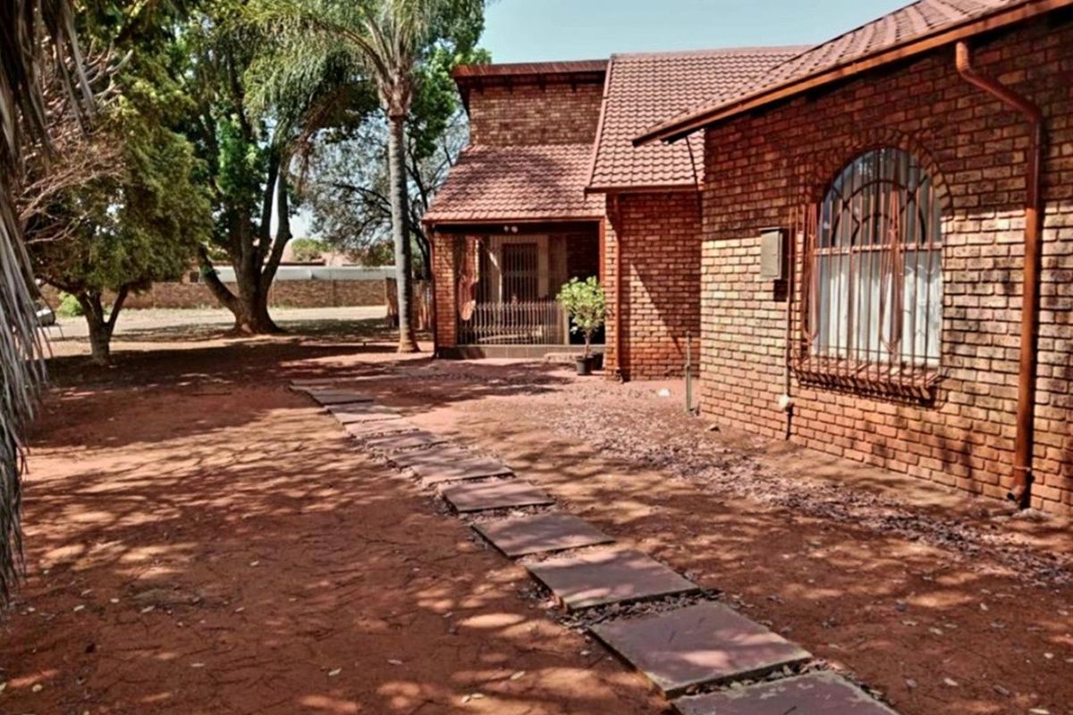 A view of the rear exterior of the house, featuring face-brick walls, tiled roofing, and a stone pathway leading through the garden area.