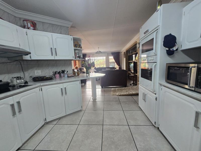 Open-plan kitchen and living area featuring white cabinetry, double wall oven, ceramic tile flooring, and a breakfast counter connecting to the lounge.