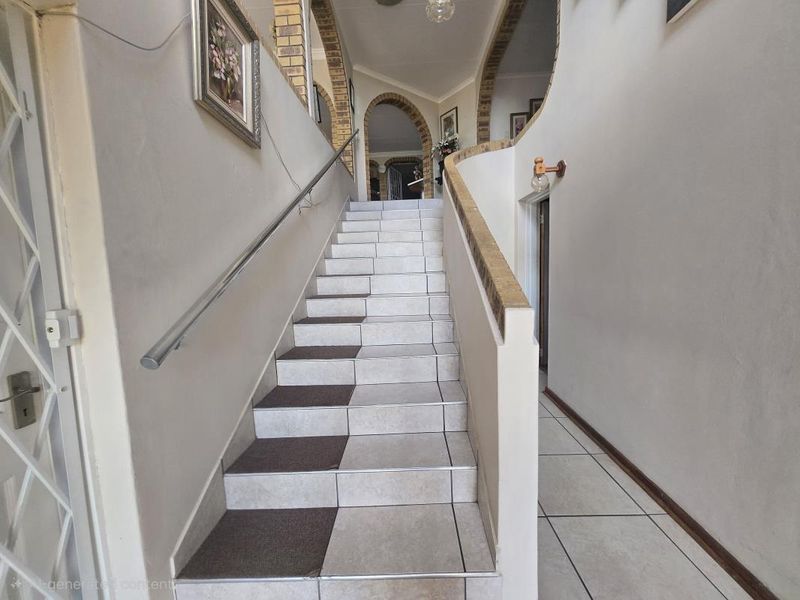 A tiled staircase with a metal handrail leading to an upper level, featuring brick archway detailing and neutral wall finishes.