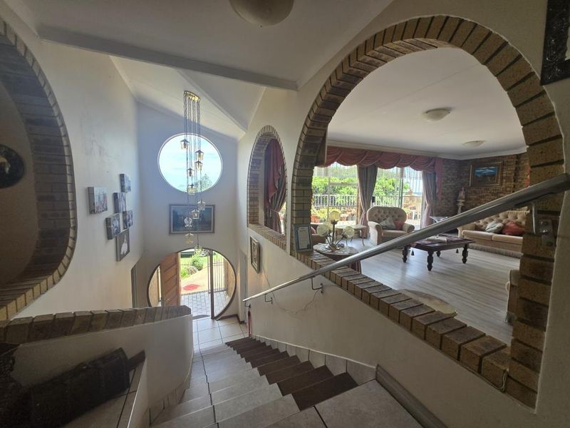 Entrance foyer featuring a staircase with brick archways, circular window, and tiled flooring, leading into an open-plan living area.