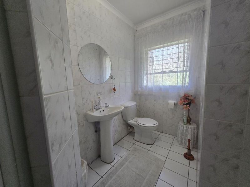 A functional bathroom featuring a pedestal basin, ceramic toilet, and fully tiled walls and flooring with a window providing natural light.