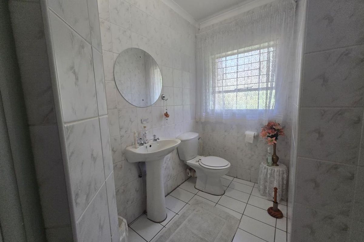 A functional bathroom featuring a pedestal basin, ceramic toilet, and fully tiled walls and flooring with a window providing natural light.