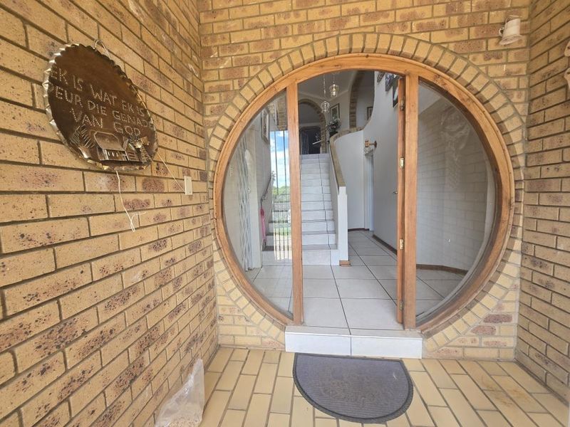 Entrance area featuring a distinctive circular timber-framed door, face-brick exterior walls, and tiled flooring leading into the home's interior staircase.
