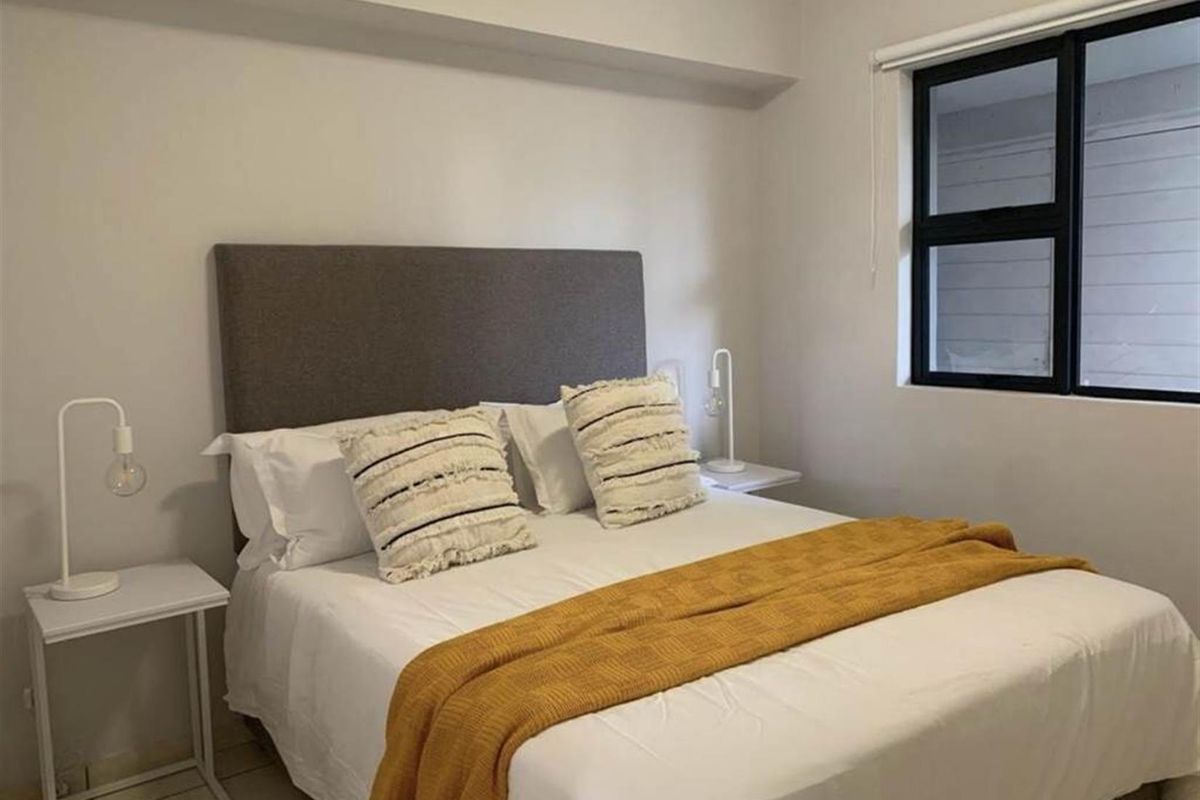 A well-maintained bedroom featuring neutral walls, tiled flooring, and a large black-framed window providing natural light.