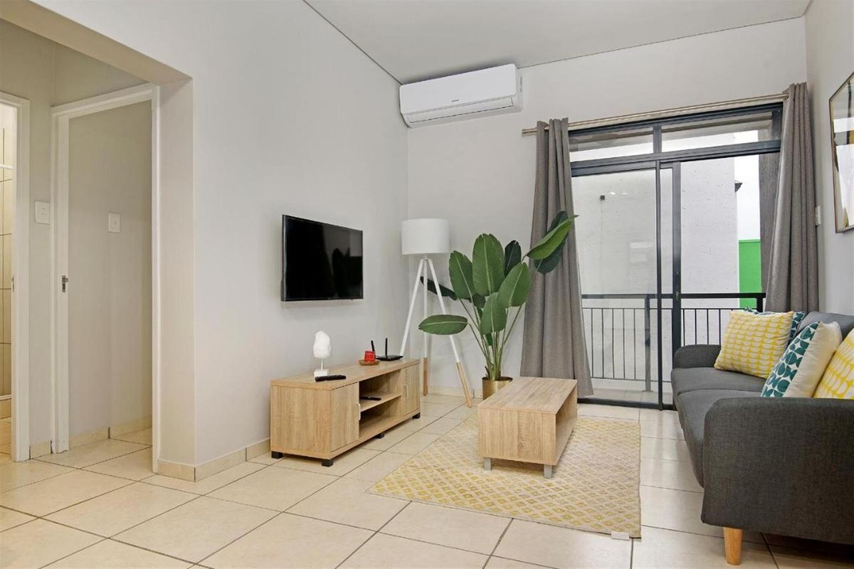 A bright and well-maintained living room featuring tiled flooring, a wall-mounted air conditioning unit, and direct access to a private balcony through sliding glass doors.