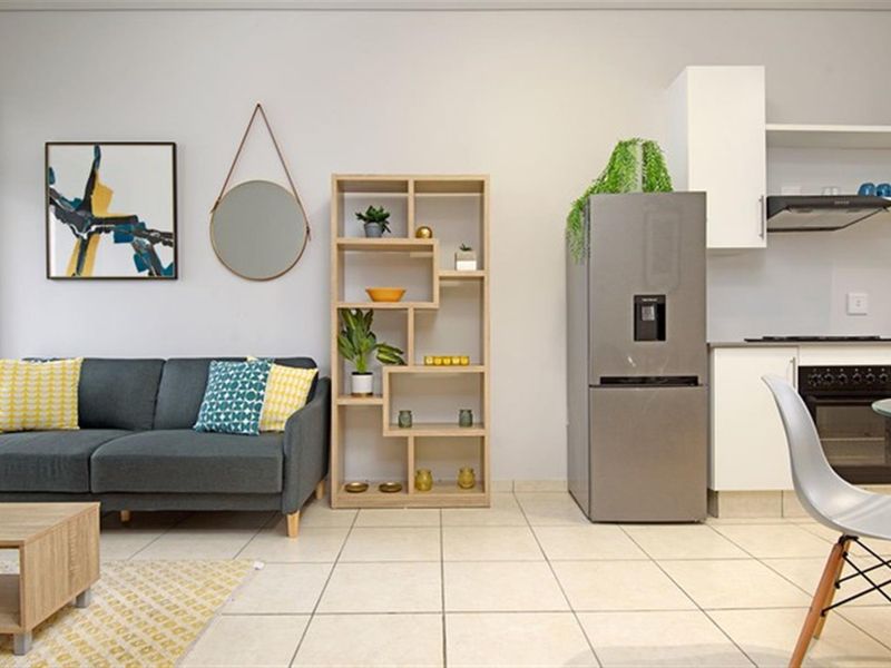 A bright open-plan living and kitchen area featuring neutral tiled flooring, modern white cabinetry, and integrated kitchen appliances.