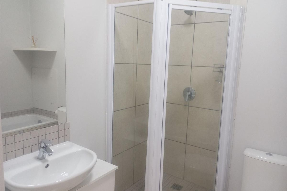 A clean and functional bathroom featuring a glass shower enclosure, vanity basin with storage cabinet, wall mirror, and a standard toilet.