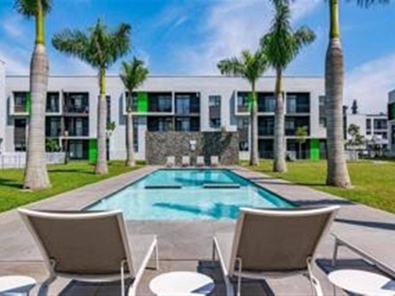 A well-maintained communal swimming pool area featuring a stone feature wall, paved deck, and landscaped garden surroundings within an apartment complex.