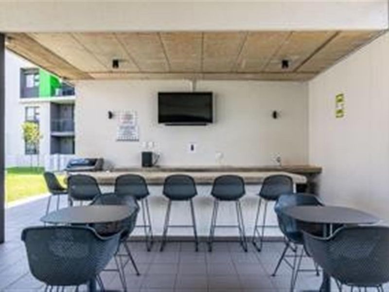 A covered outdoor patio area featuring a built-in bar counter, tiled flooring, and an exposed concrete ceiling, ideal for social gatherings.