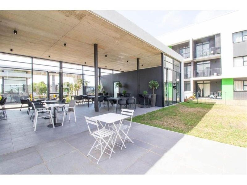A modern covered patio area featuring a concrete ceiling, tiled flooring, and extensive glass walls, providing a seamless transition to the outdoor garden space.