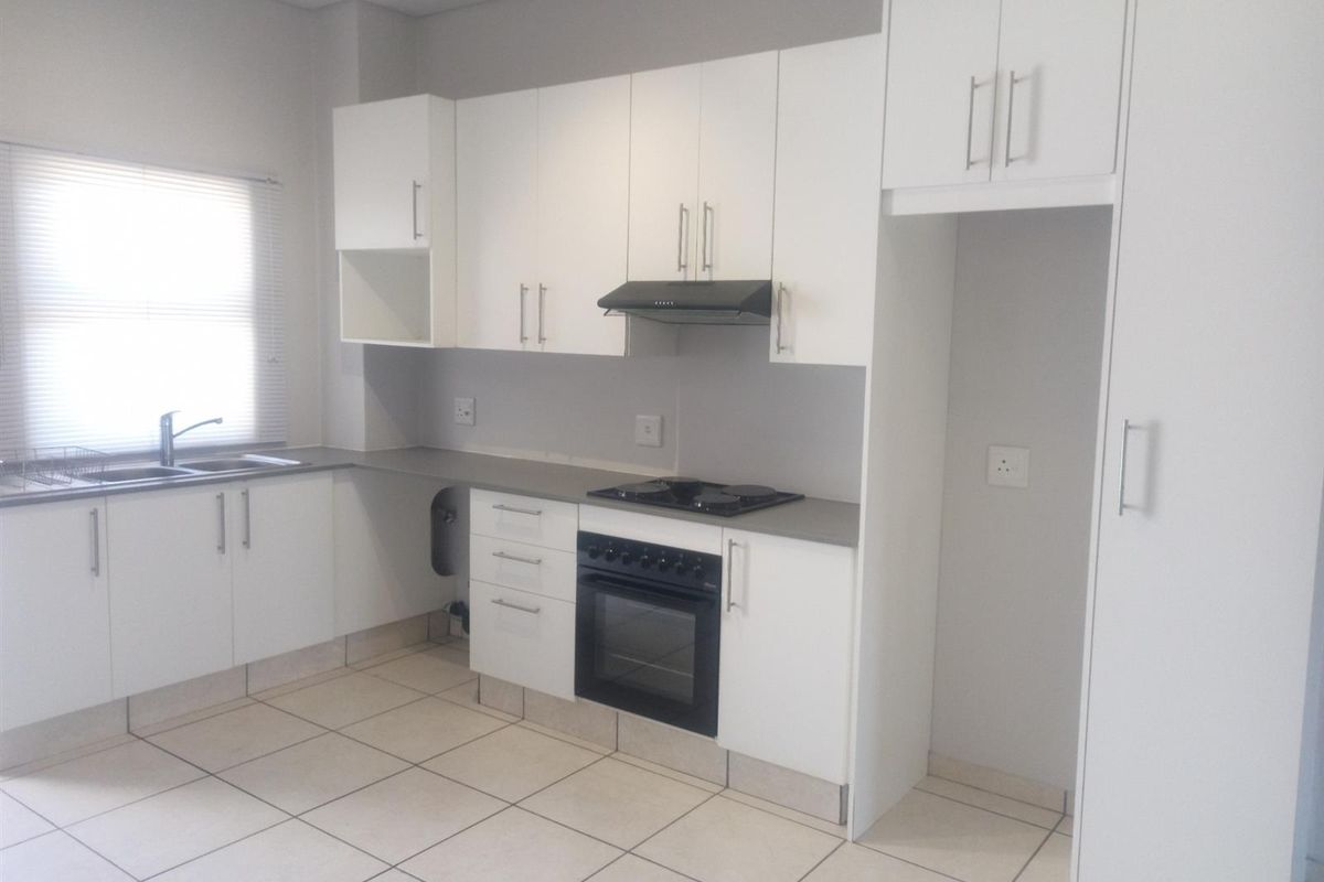 A clean, functional kitchen featuring white cabinetry, built-in oven and hob, tiled flooring, and a dedicated space for a refrigerator.