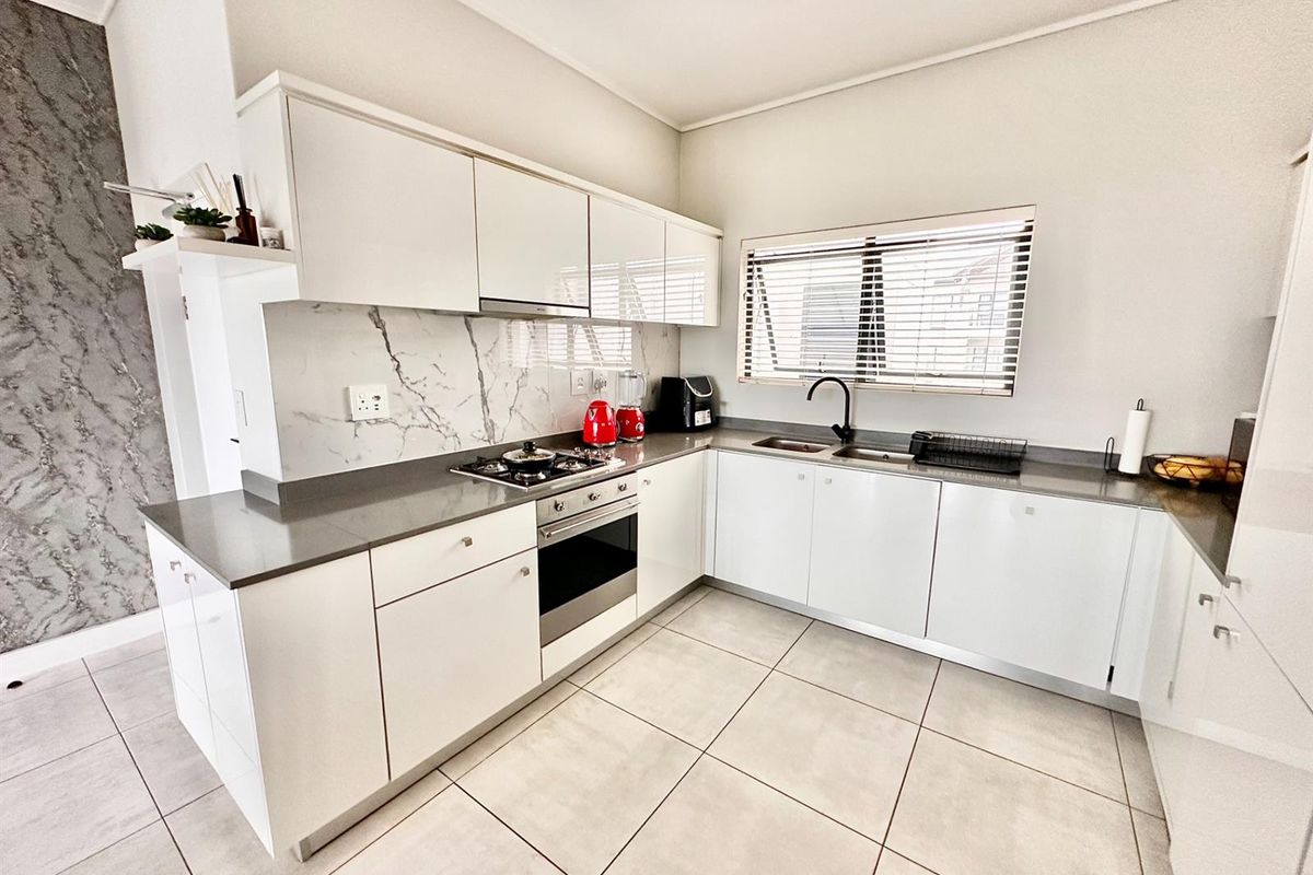 Modern kitchen featuring white cabinetry, stone countertops, marble-look splashback, gas hob, built-in oven, and tiled flooring.