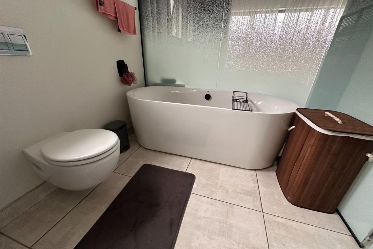 Modern bathroom featuring a sleek freestanding bathtub, wall-hung toilet, and a frosted glass privacy partition with neutral floor tiling.