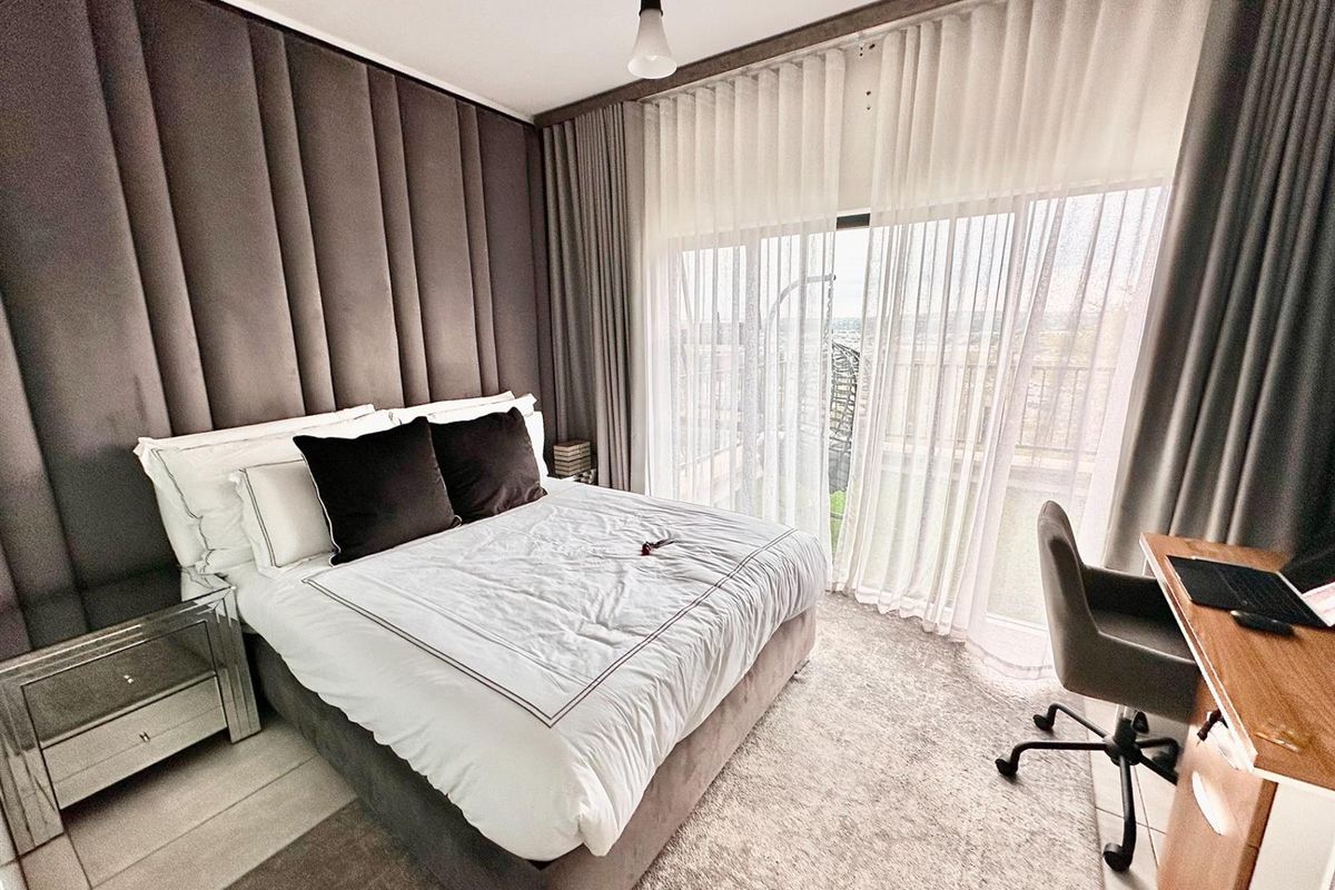 Modern bedroom featuring floor-to-ceiling upholstered wall paneling, neutral carpeting, and large sliding glass doors providing access to a private balcony.