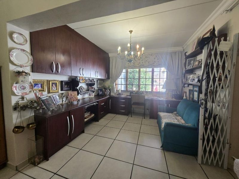 A functional home office featuring extensive built-in dark wood cabinetry, a dedicated desk area, tiled flooring, and a security gate at the entrance.