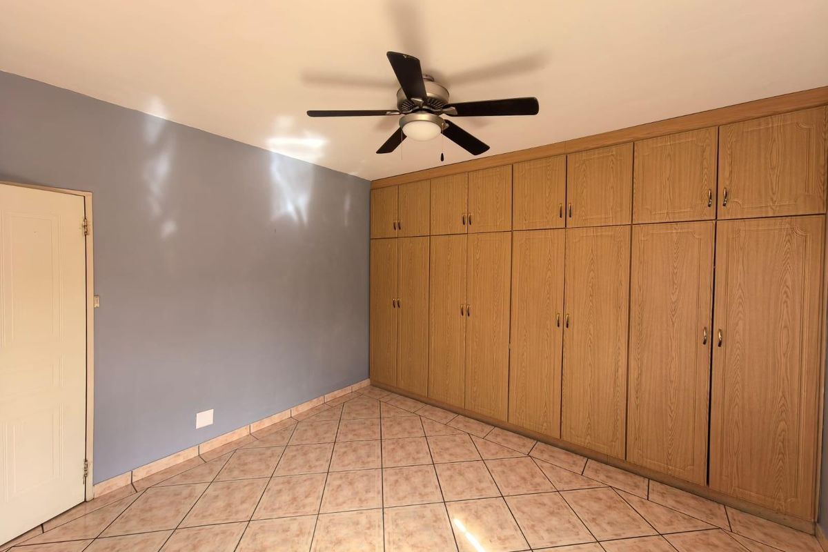 A bedroom featuring extensive built-in wooden cabinetry, tiled flooring, and a ceiling fan.