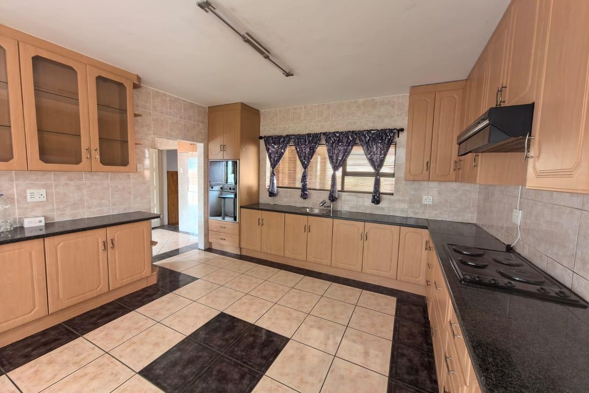 Spacious kitchen featuring light wood cabinetry, dark granite countertops, integrated oven, hob, extractor fan, and tiled flooring with a decorative pattern.