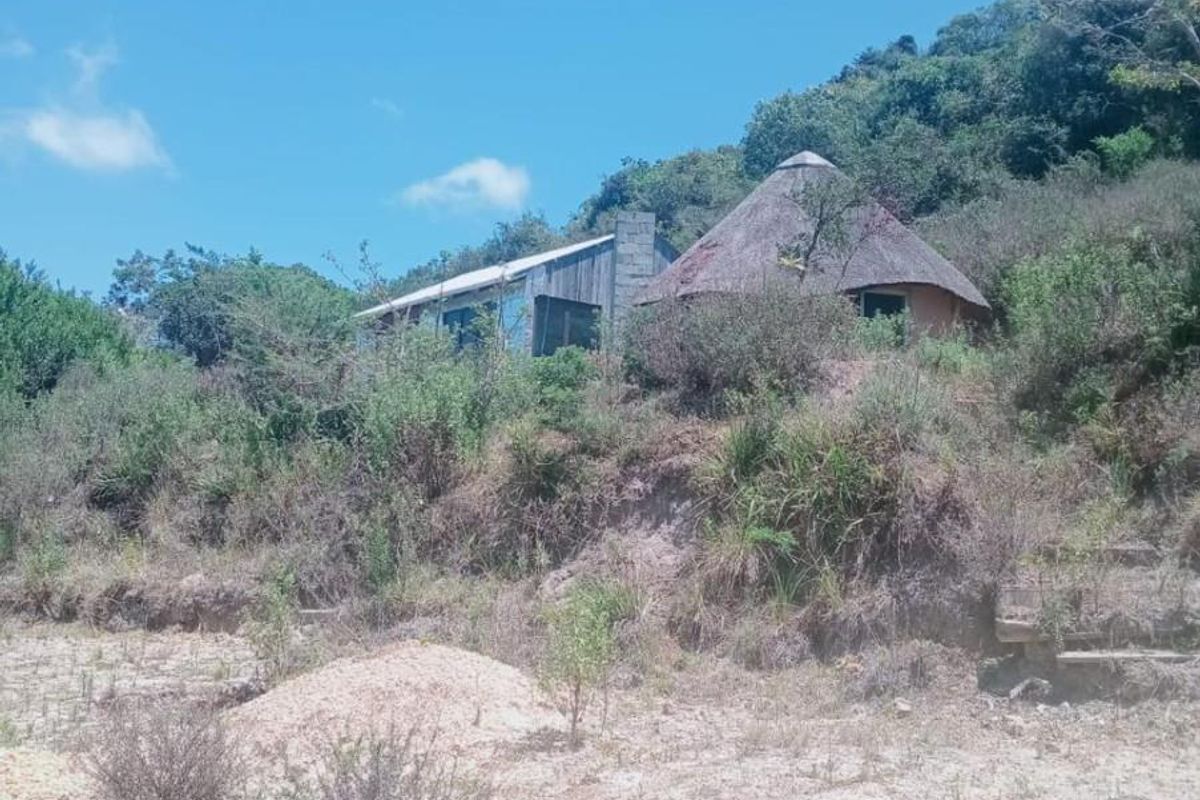 A rustic farm property featuring a traditional thatched-roof structure nestled into a hillside, surrounded by natural landscape and native vegetation.