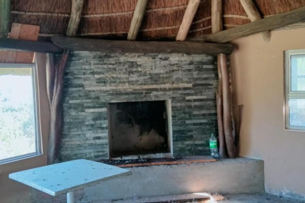 Rustic living area featuring a traditional thatched roof, exposed timber beams, and a stone-clad built-in fireplace in a farm-style setting.